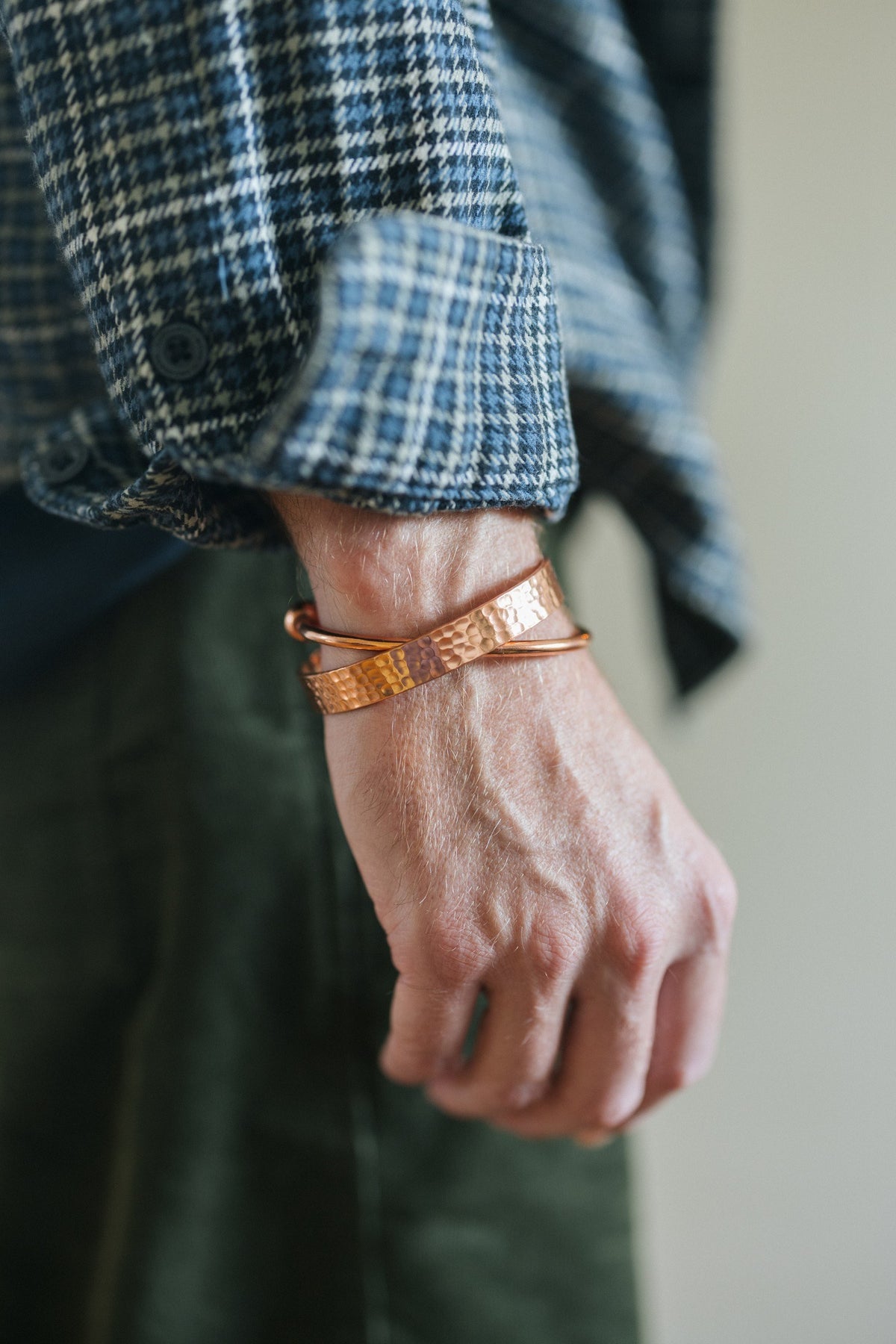 Kopero Kobberarmbånd Hamret, om håndleddet over en ternet skjorteærme, sammen med et glat armbånd
