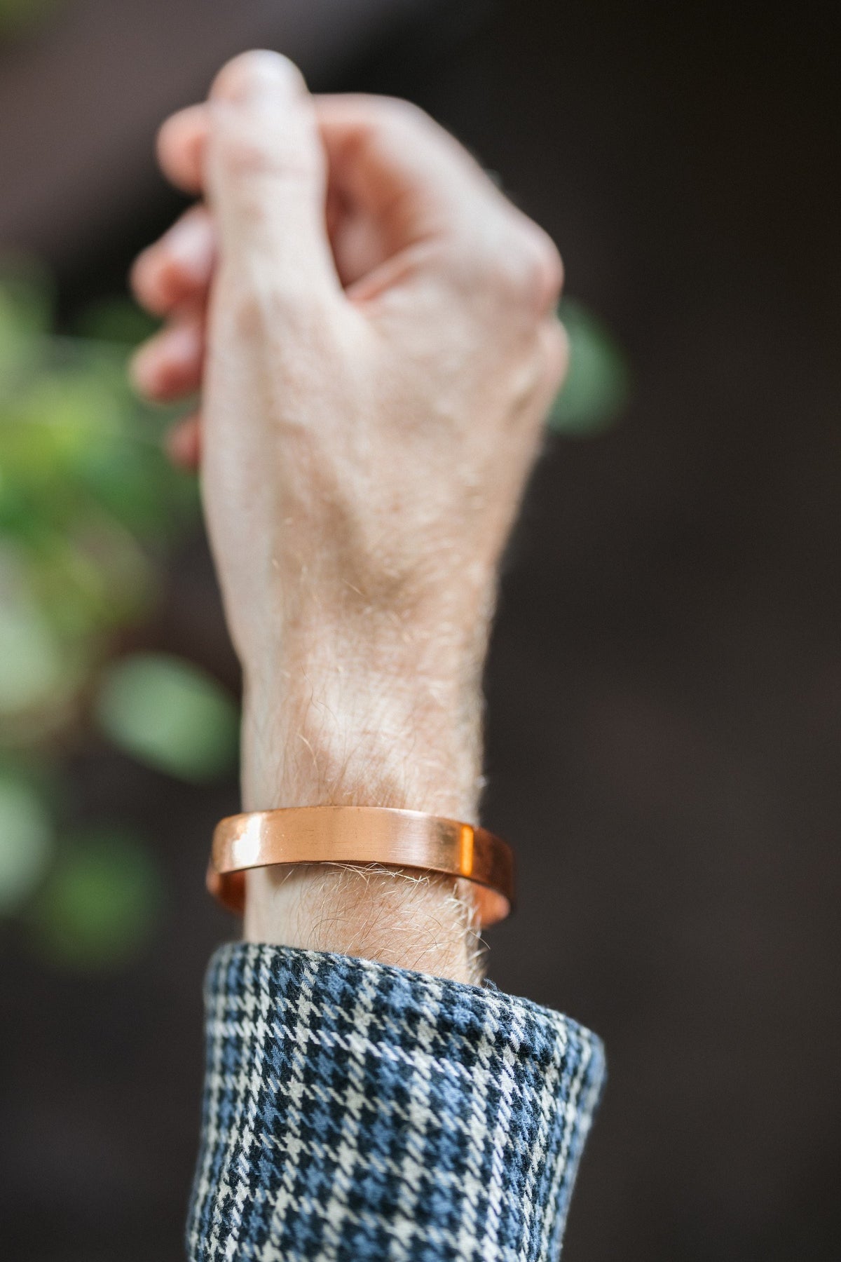 Kopero Kobberarmbånd Glat, om håndleddet, med hånden løftet mod en mørk baggrund